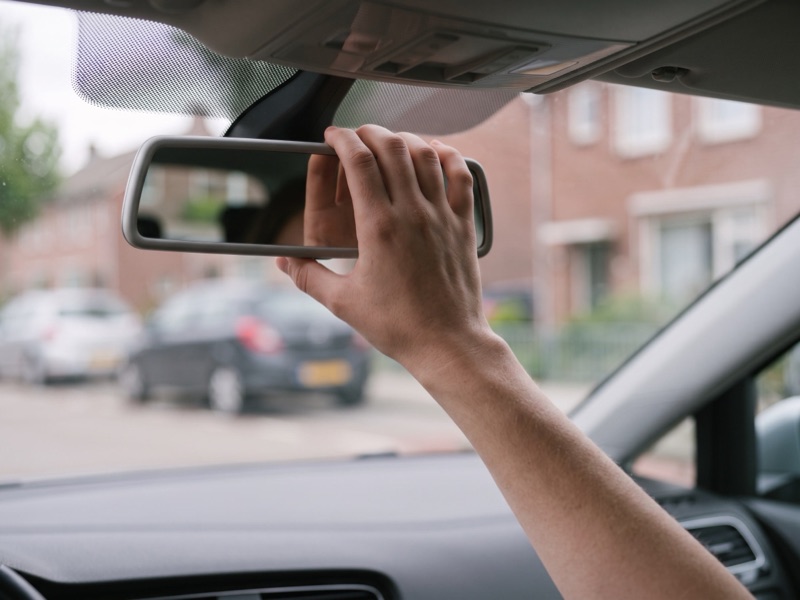 Close-up van een hand die de binnenspiegel goed zet, met de straat wazig op de achtergrond